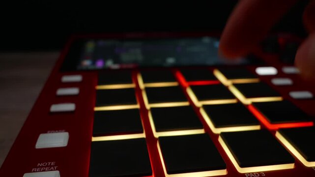 Musician finger taps patterns on illuminated pads of a red drum machine. Concept of electronic music production, creative audio engineering, and professional studio workflow.