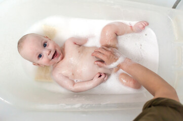 Fototapeta premium Joyful bath time moment with a bubbly baby enjoying fun water splashes in a cozy home setting. The atmosphere is filled with laughter and warmth