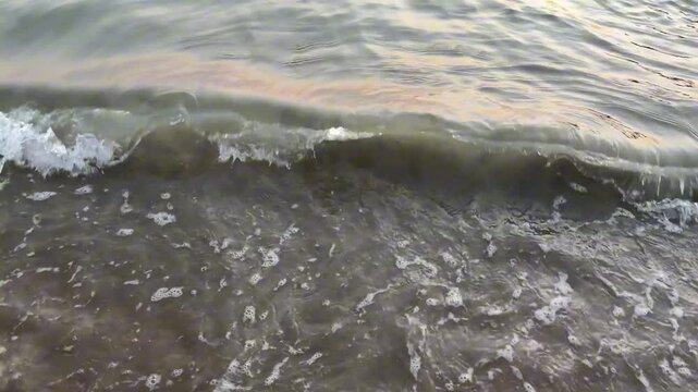 Cinematic 4K 120fps slow-motion close-up of a small ocean wave curling and breaking. The smooth water reflects warm golden hour light before crashing into white foam.