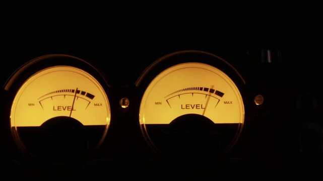 Close-up of two round, backlit analog VU meters with needles moving to measure sound levels. Concept of vintage audio technology, music production, and precision measurement.