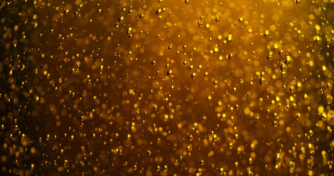 Abstract golden bubbles rising in liquid with sparkling highlights and soft bokeh. Macro texture resembling carbonation in beer, champagne or sparkling beverage creating a luxurious glowing backgrou