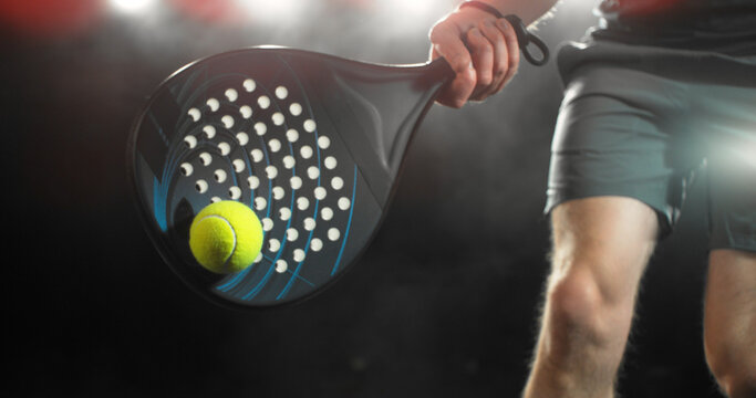 Dynamic action shot of a padel player hitting a yellow ball with a racket during a match. Speed and power, capturing the energy and intensity of modern racket sports