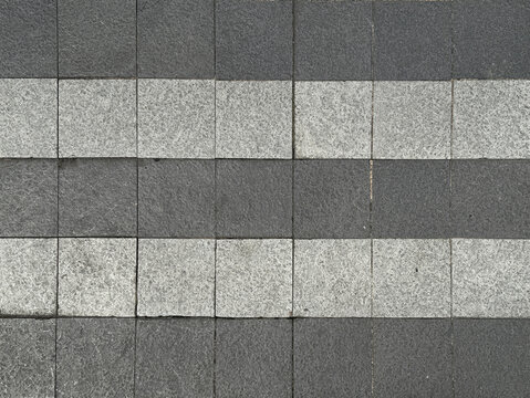 Black and grey square paving outdoor stone tiles with random shades and roughness. Suitable for exterior garden flooring. Seamless background texture.