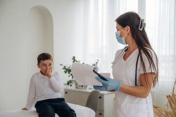 Obraz premium Writing notes into notepad. Boy is in routine appointment in clinic with female doctor