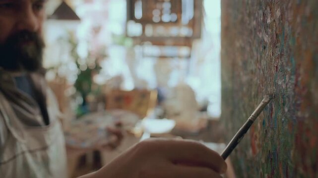 Male painter applying fine brush strokes to canvas in art studio, working on expressive abstract composition. Close up view