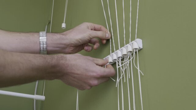 A man adjusts cords of a ceiling clothes dryer, securing plastic stoppers into a wall holder. Concept of laundry routine, home organization, housekeeping, and convenient domestic appliances.