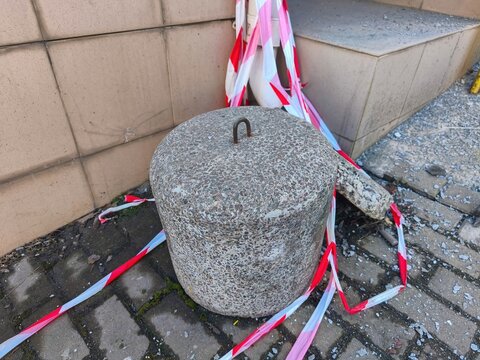 Cylindrical granite barrier block standing on urban sidewalk with red white caution tape marking restricted construction area