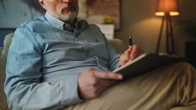 Experienced male psychologist writing notes during private therapy session