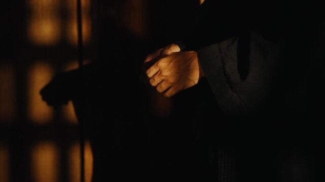 Person praying with rosary beads in a dark confession booth