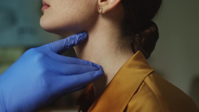 ENT specialist in gloves examining female patient's throat and lymph nodes