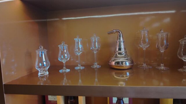 Crystal crystalware and decanters lined on lit wooden shelf, reflecting warm gold light, elegant, polished barware display evoking luxury, craftsmanship and refined home or club ambiance