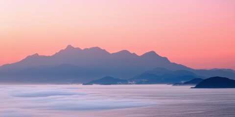 Fototapeta premium Mountains rise above mist, bathed in soft pink sunset hues. Calm water reflects light, creating serene landscape.