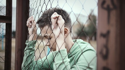 cinematic sad boy stands alone head bowed near the fence, frustrated boy dropped eyes, regrets the act, have fun and enjoy © vla
