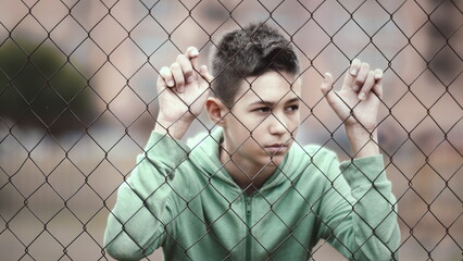 refugee boy stands alone head bowed near the fence, frustrated boy dropped eyes, regrets the act, have fun and enjoy © vla