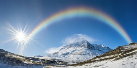 Fototapeta premium Bright rainbow arcs over snowy mountains. Sun shines intensely, illuminating landscape. Beautiful natural scenery presents calm vista.