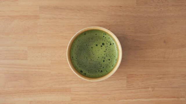 木目テーブルの上の抹茶碗 真上からの俯瞰動画 日本の伝統と禅 / Matcha green tea in a bowl on wooden table, bird's eye view video, Japanese Zen concept
