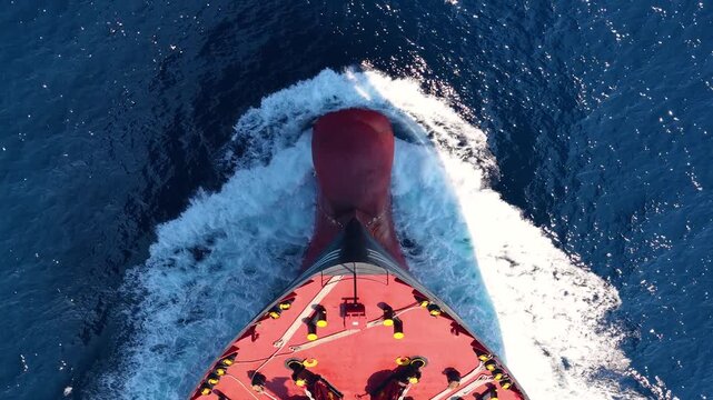 Aerial overhead close-up view of a bow from a large container cargo or tanker ship sailing with speed over the ocean