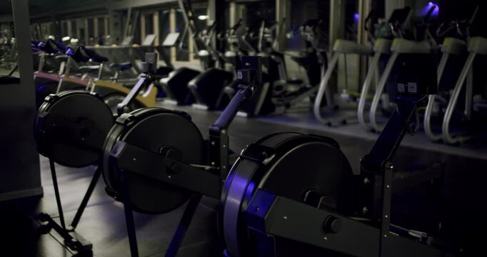 Dark and moody gym with rows of modern rowing machines and fitness equipment for cardio training, ready for an intense workout and promoting a healthy lifestyle in a fitness club