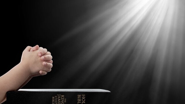 Christian child hand praying over Bible on dark background
