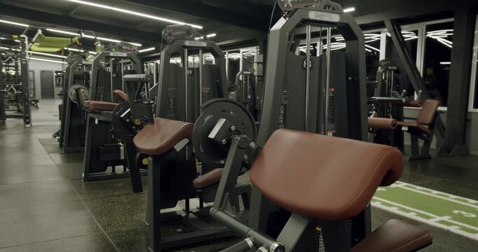 Slow motion tracking shot revealing rows of professional strength training machines and exercise equipment inside a spacious, modern, and empty gym facility, ready for a workout session