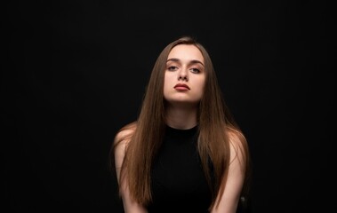 Fototapeta premium Young woman with natural long hair and serious expression posing on plain black background, portraying beauty and strength