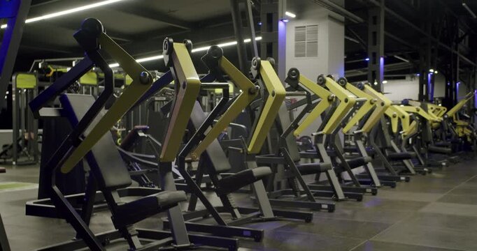 Slow motion wide shot of an empty modern gym interior with a row of professional strength training machines ready for a workout session, showcasing the fitness club's available equipment