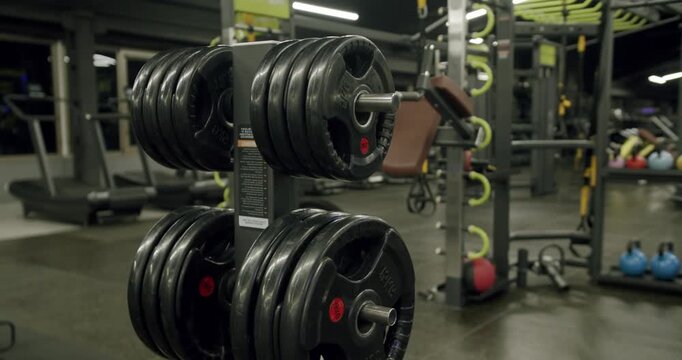 Weight plates on a stand inside a modern and empty gym, with various fitness machines and equipment blurred in the background, showcasing a space dedicated to bodybuilding and strength training