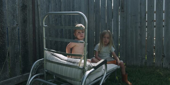 Two children sitting on a sun lounger in a field
