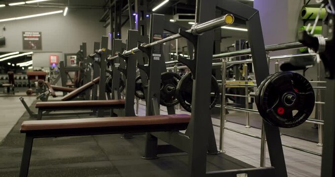 Modern fitness club interior with a row of bench presses and barbells ready for a workout. The empty gym features professional equipment for strength training, bodybuilding, and weightlifting