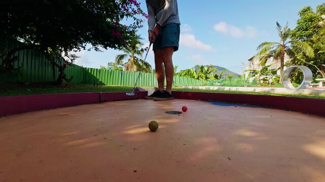 Amateur Golfer Misses Short Putt Near Hole on Mini Golf Course in Tropical Park, Low Angle View of Player Holding Putter While Ball Stops Beside Target, Outdoor Recreation And Beginner Practice