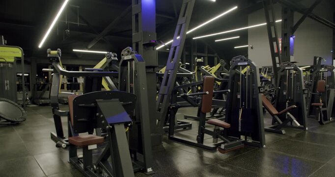 Empty modern gym interior featuring a variety of professional strength training machines and fitness equipment, illuminated by stylish ceiling lights in a dark, contemporary setting