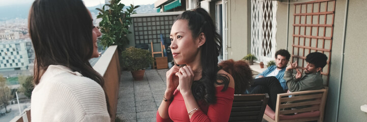 Fototapeta premium Two girls, friends chat while standing on the balcony on the modern city on the background. Panoramic