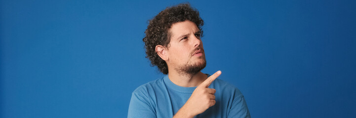Guy with curly hair dressed in blue t-shirt is thinking over difficult choice, imagining plan in...