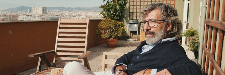 Fototapeta premium Middle-aged man enjoying sunny weather on the balcony. Panoramic