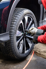 Worker changes tire on a black vehicle at a garage during daylight hours using a power tool