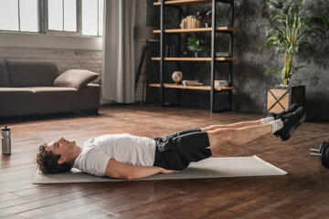 Domestic fitness success. Smiling young man lie on back on gymnastic mat at living room do core...