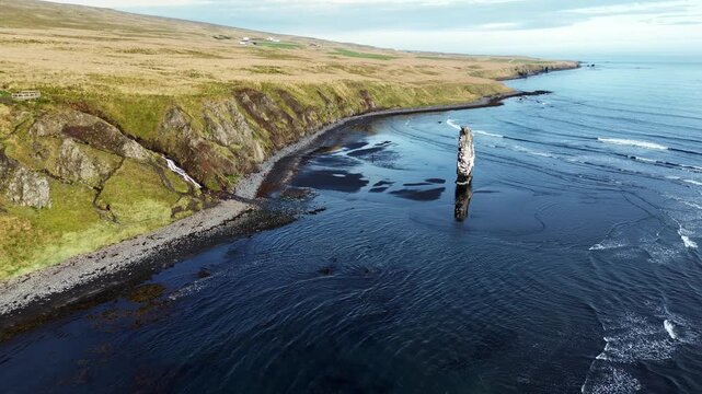 Aerial drone view of Hvitserkur, the famous basalt sea stack rising from the ocean along the Vatnsnes Peninsula in northern Iceland. Waves gently roll across the black sand beach while cliffs and gras