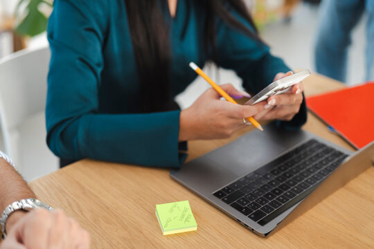 A person uses a smartphone and pencil at a desk with a laptop and notepad, focusing on financial planning and task management.