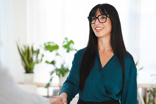 A smiling woman in glasses shakes hands with someone, signifying a successful business meeting or a new partnership.