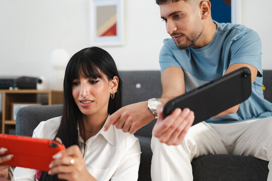 A man and a woman are playing a video game together on a handheld console in a living room.