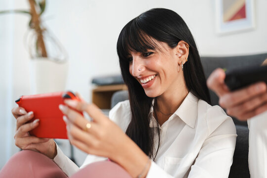 A young woman smiles while playing a video game on a portable console, enjoying a moment of leisure at home.