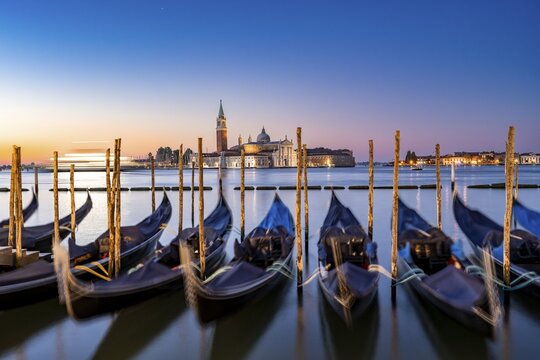 Venetian gondolas, boat dock at St Mark's Square, church of San Giorgio Maggiore in the background, long exposure at sunrise, Venice, Veneto, Italy