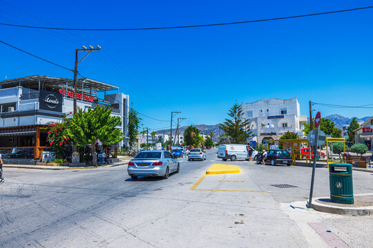 Beautiful view of town street with cars buildings and mountains against clear blue sky background. Greece. 