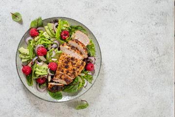 Fresh salad with grilled chicken, avocado, and raspberries served on a plate © azurita