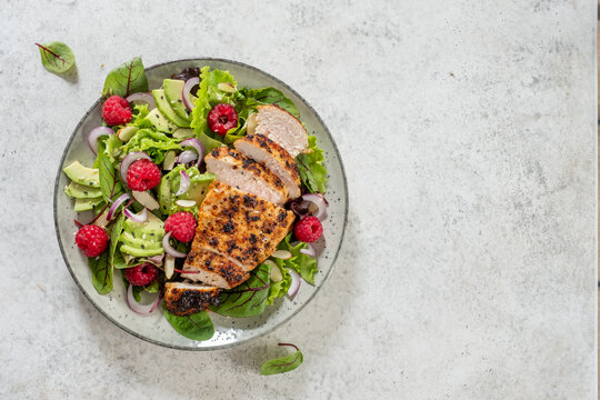 Fresh salad with grilled chicken, avocado, and raspberries served on a plate