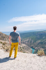 Fototapeta premium Man Stands at the Edge of Sulak Canyon Looking Over the Steep Cliffs and River Below During a Sunny Day
