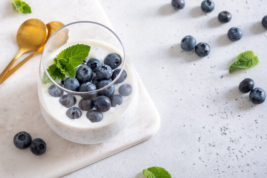 Fresh Yogurt With Blueberries and Mint Served in a Glass on a Table With Golden Spoons