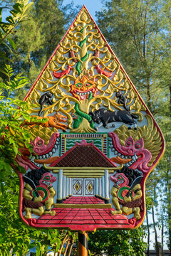 Colorful Javanese Gunungan Kayon carving with intricate details of mythical animals, guardians, and the tree of life against a natural forest background. Traditional folk art and cultural symbol.