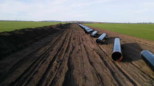 Ground-level perspective of steel pipes for the Balkan Stream gas pipeline in Bulgaria. Row of large diameter tubes on a construction site across green fields under a clear sky