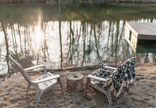 A chair with a cozy blanket  by a pond at sunrise.